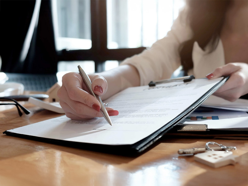 real estate agent assisting client to sign contract paper at desk with house model