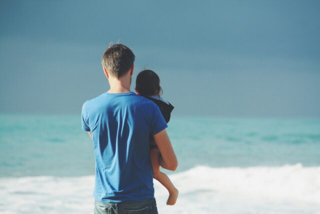 dad standing at ocean with child