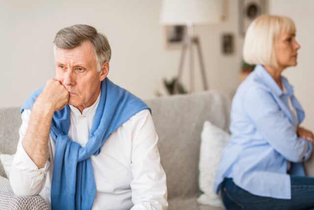 Relationship problems. Senior couple after argument sitting on opposite sides of sofa